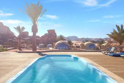 a swimming pool in a resort with a palm tree at Palmera Camp Wadi Rum in Wadi Rum