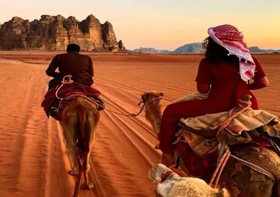 a man and a woman riding on camels in the desert at Wadi Rum in Wadi Rum