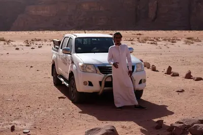 a man standing next to a white truck in the desert at Wadirum momoo in Wadi Rum