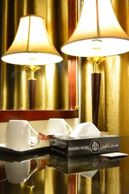 two lamps on a table with a book and two cups at Rakeen Hotel in Amman