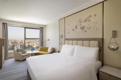 a hotel room with a white bed and a table at Signia by Hilton in Amman