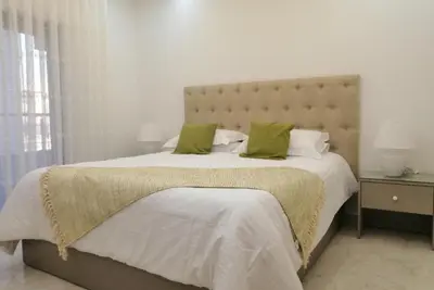 a white bedroom with a large bed with green pillows at Amazing one Bedroom Apartment in Amman Elwebdah 1 in Amman