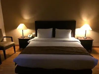 a bedroom with a large bed with two lamps and a chair at Shepherd Hotel in Amman
