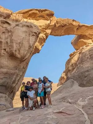 a group of people standing under a rock formation at Shahrazad desert, Wadi Rum in Wadi Rum