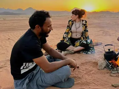 a man and a woman sitting around a fire in the desert at Shahrazad desert, Wadi Rum in Wadi Rum