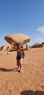 a woman carrying a surfboard on her head on the beach at Shahrazad desert, Wadi Rum in Wadi Rum
