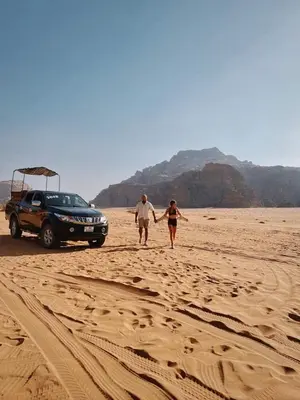 a man and woman walking on a beach with a car at Shahrazad desert, Wadi Rum in Wadi Rum