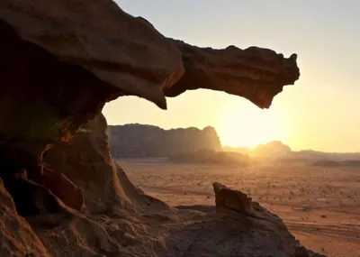 a rock in the desert with the sunset in the background at Abdullah desert trips in Wadi Rum