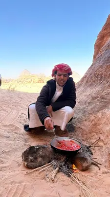 a man sitting on the beach cooking food over a fire at Abdullah desert trips in Wadi Rum