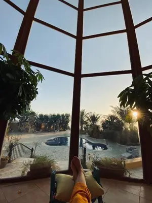 a person laying in a chair looking out a window at a pool at The Precious Villa in Sowayma