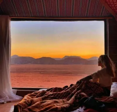 a woman laying in bed looking out of a window at moon city with jeep trips in Wadi Rum