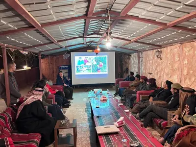 a group of people sitting in a room watching a presentation at Petra Bedouin House 1 Attallah guest house in Wadi Musa