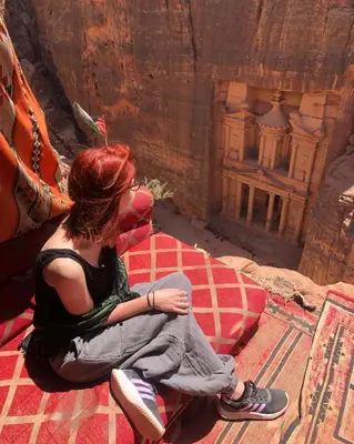 a woman sitting on a bed looking down at a building at Petra Bedouin House 1 Attallah guest house in Wadi Musa