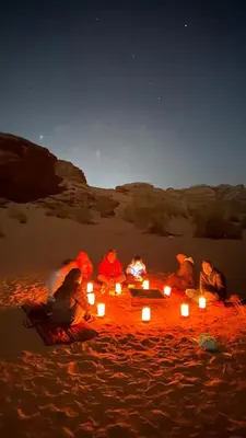 a group of people sitting around a bonfire on the beach at night at Bubble RumCamp in Wadi Rum