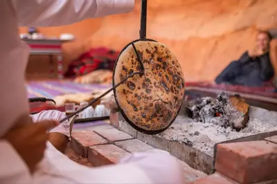 a person holding a frying pan over a fire at Wadi Rum Cave Camping in Wadi Rum