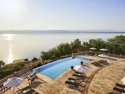 a swimming pool with chairs and umbrellas next to the water at Mövenpick Resort & Spa Dead Sea in Sowayma