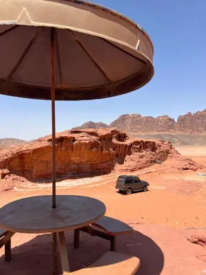 a table with an umbrella and a car in the desert at Art Camp Wadi Rum in Wadi Rum