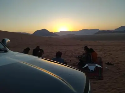 a group of people sitting in the desert watching the sunset at rum rema camp in Wadi Rum