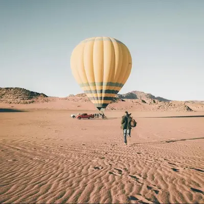 a person walking in the desert with a hot air balloon at rum rema camp in Wadi Rum
