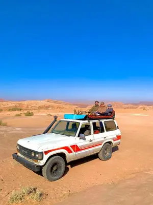 two people sitting on top of a white truck in the desert at Wadi Rum Trail in Wadi Rum