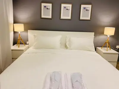 a bedroom with a large white bed with two lamps at Elite Corner Apartment in Ţāb Kirā‘