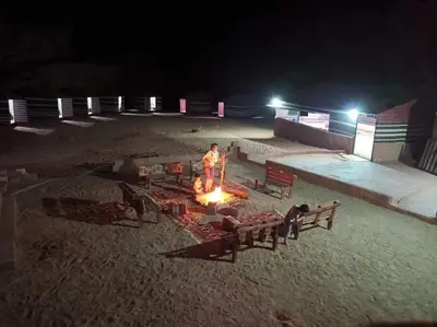 a man standing around a fire on the beach at night at Wadi Rum White Mountain Camp in Wadi Rum