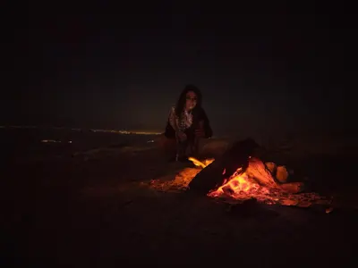 a woman sitting next to a fire at night at private room with cultural experience and great landscapes in Şirfah