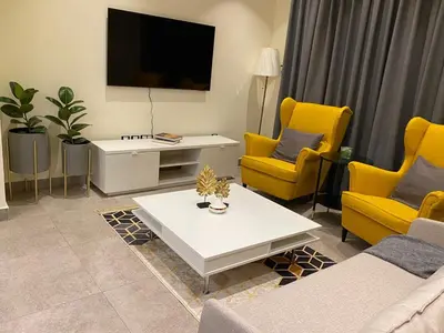 a living room with yellow chairs and a tv at Luxury Apartment in DAMAC Towers in Amman