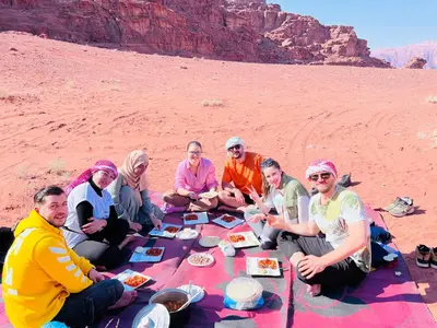 a group of people sitting on a picnic blanket in the desert at Wadi rum Bubble Camp & tour in Wadi Rum