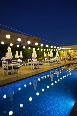 a restaurant with tables and chairs and a pool at night at Aitch Boutique Hotel - an LIH Hotel in Madaba