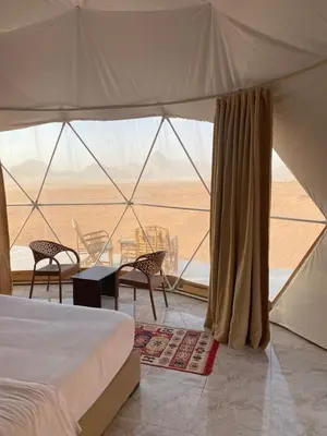 a tent with a bed and a table and chairs at Qimam Al Sarab Camp Wadi Rum in Wadi Rum