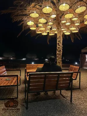 a man sitting on a bench under a tree at Rum Four Seasons luxury Camp & Jeep Tours in Wadi Rum