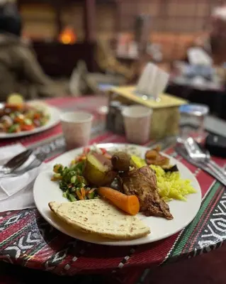 a plate of food with meat and vegetables on a table at Wadi Rum Trip Bedouin Camp in Wadi Rum