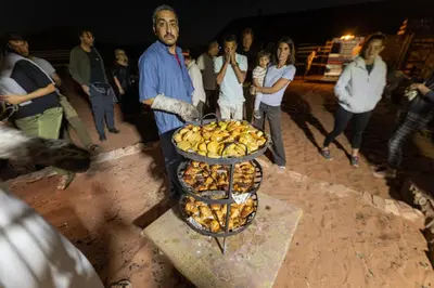a man standing next to a grill with a bunch of food at Wadi Rum Trip Bedouin Camp in Wadi Rum