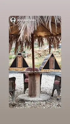 a table and chairs under an umbrella with tents at Wadi Al-Hassa camp in Khawkhah