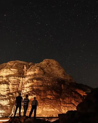 a group of three people standing under a night sky at stars magic camp in Wadi Rum