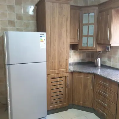 a kitchen with a white refrigerator and wooden cabinets at شقة مفروشة في ام اذينة in Amman