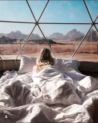 a person laying in bed looking out at the desert at Katrina Rum camp in Wadi Rum