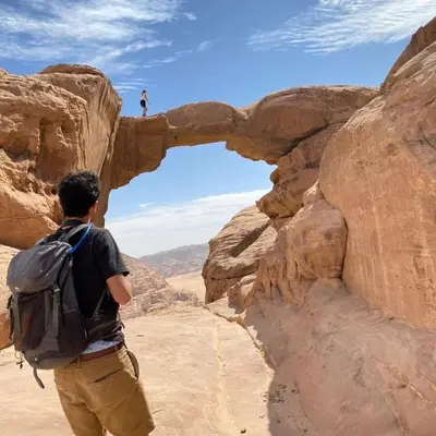 a man with a backpack walking through an arch in the desert at The sun of Wadi Rum in Wadi Rum