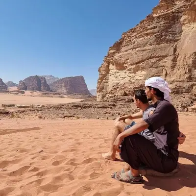 two people sitting on the sand in the desert at The sun of Wadi Rum in Wadi Rum