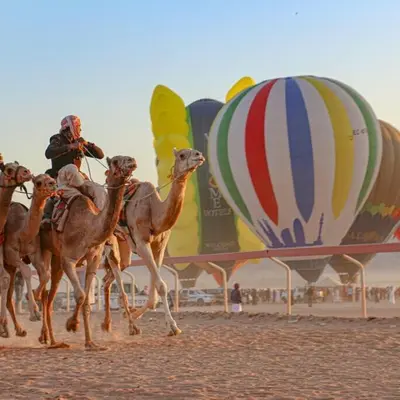 a group of camels running on a beach with hot air balloons at The sun of Wadi Rum in Wadi Rum
