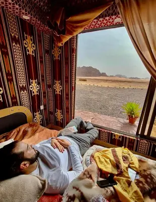 a man laying on a bed in a train at Bedouin Desert Life Camp & Jeep Tours in Wadi Rum