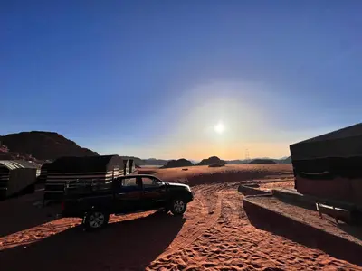 a truck parked in the desert with the sun setting at Wadirum Zeid Classic camp in Wadi Rum