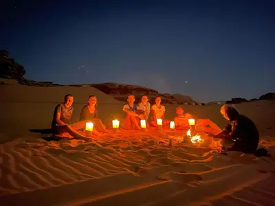 a group of people sitting around a fire in the sand at Wadi Rum Star Camp in Wadi Rum