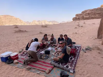 a group of people sitting on a blanket in the desert at Wadi Rum Star Camp in Wadi Rum