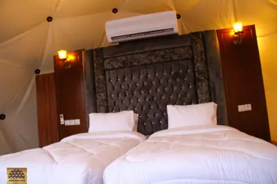 two beds with white sheets and a tv on top at Jabal Rum Camp in Wadi Rum