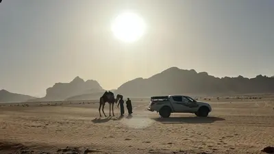a couple of people and a camel and a car in the desert at Jabal Rum Camp in Wadi Rum