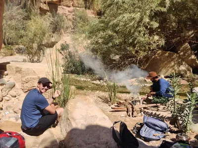two men sitting on rocks next to a fire at 7 Caves Hotel in Al Jāyah