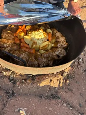 a pan filled with meat and vegetables on the ground at Night Magic Camp in Wadi Rum