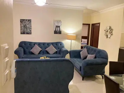 a living room with a blue couch and two chairs at Uptown Hotel Apartment in Amman